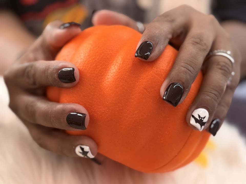 Glossy short black nails with a white bat accent, holding an orange pumpkin